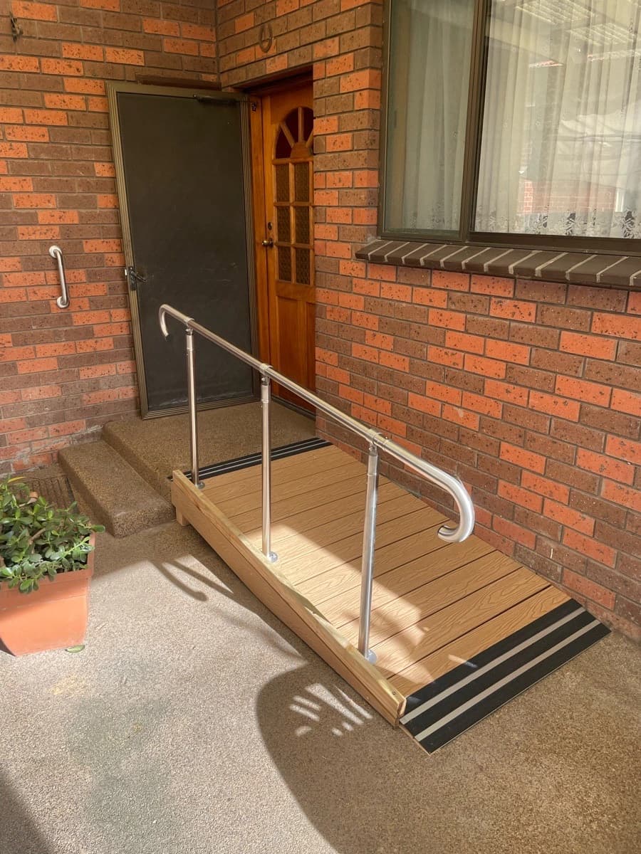 After: a timber access ramp with a stainless steel handrail running along a brick wall