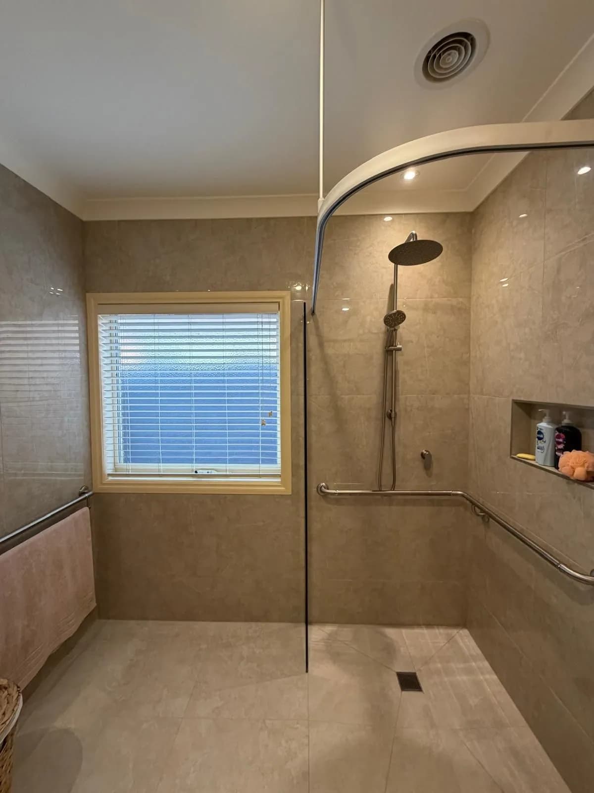 A level-access shower with a curved shower rail, a wall-mounted grab rail, and a recessed shelf, opening onto the floor